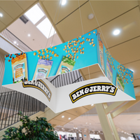 An advertising hanging display features 'Ben & Jerry's' brand with ice cream images, suspended in a mall's interior.